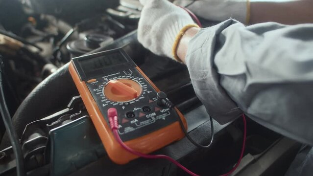 Close up of hands of specialist using multimeter to check engine work at car service