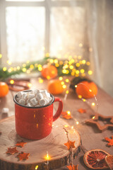 Cute cozy winter composition. red mug, marshmallows, oranges and Christmas lights.