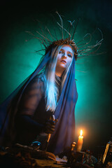 Witch concept. Woman sorceress in the mantle in the candle light on the dark background.