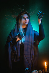 Witch concept. Woman sorceress in the mantle in the candle light on the dark background.
