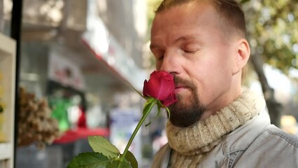 An attractive Caucasian man sniffed a red rose and holding the flower smiles sweetly and looks at the camera. Give flowers to the woman you love on Valentine's Day. Handsome men