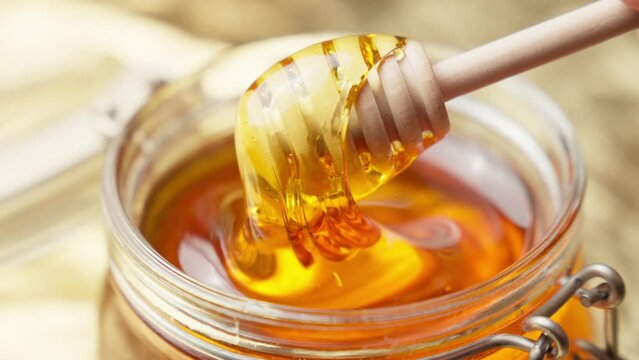 Honey dripping. Dipping honey with honey scoop in glass jar. Healthy organic food. Thick honey dripping from wooden spoon. Close-up in 4K, UHD