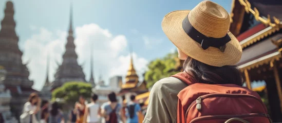 Fototapeten Asian woman backpacker taking selfies and pictures in the city. A young girl traveler recording vlogs on her holiday trip to a Buddha temple in Thailand. © TheWaterMeloonProjec