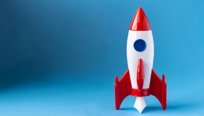 Foto op Canvas A red and white toy rocket on a blue background © Donald