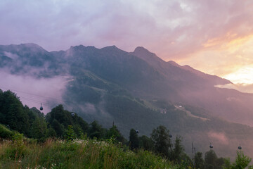 Fog and clouds in the mountains against the backdrop of the setting sun, changeable weather in the...