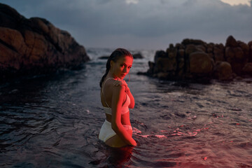 Attractive woman enjoys nighttime swim in ocean illuminated by red light, evoking a sense of...