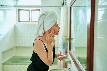 Woman in vintage bathroom applies moisturizer to face. Skincare routine, pampering at home. Beauty treatment, self-care with nourishing cream, reflection in mirror. Daily facial regimen in home.