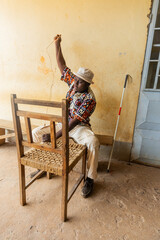 Weaving seat of a wooden chair by a blind African man. Blindness handcraft concept
