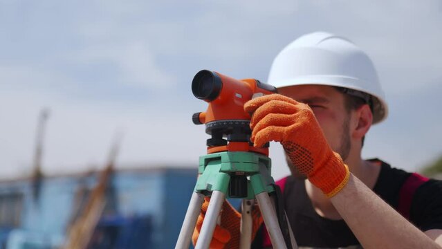 Close up shot of professional Construction Worker Using Theodolite Surveying Optical Instrument. Man wearing hard hat and work gloves measures angles for building plans.