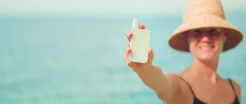 Woman demonstrating white tube of sunscreen skin care cream on sea ocean background. Girl holds a jar of cosmetic product in hand.