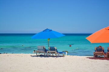 Blue sea, beautiful beach with colourful parasols and people on sun loungers on a Summer day. Tropical background.