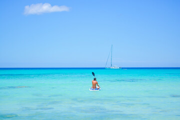 Fototapeta na wymiar A beautiful view of a person paddle boarding and a yacht in azure blue Caribbean Sea. 