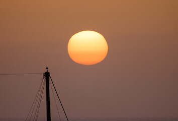A beautiful bright sunset on the ocean, a huge sun setting behind the horizon against the background of the silhouette of a ship’s mast and a bird on it. Fuerteventura, Canary Islands.