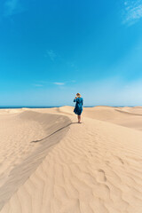 A woman hikes through sand dunes of Maspalomas, Gran Canaria, Spain - obrazy, fototapety, plakaty