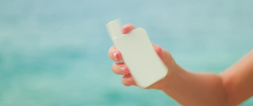 Mineral sunscreen zinc oxide shake well before use. Girl hand holding white tube jar of skin care cream on ocean sea water background.