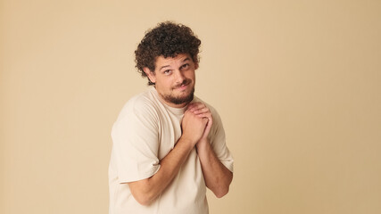 Guy with curly hair and freckles, feels hesitant holds his hands together looks at the camera has...