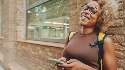 Saughing woman with backpack texting on mobile phone while standing outside