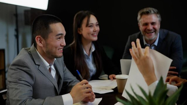 Confident young chinese businessman minded looking introduction diagrams papers. Three business people discuss about numbers year reports. Young man interested listening speech of financial director