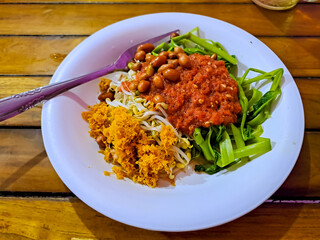 Plecing Kangkung, an indonesian dish from Lombok island. Boiled water spinach and bean sprouts served with  tomato sambal, fried peanuts and seasoned grated coconut