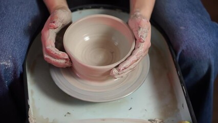 Promoting the ideals of emission-free and home-based production. Female artisan's hands with red manicured nails shapes a clay bowl on a rotating metal pottery wheel. Top view of sitting woman