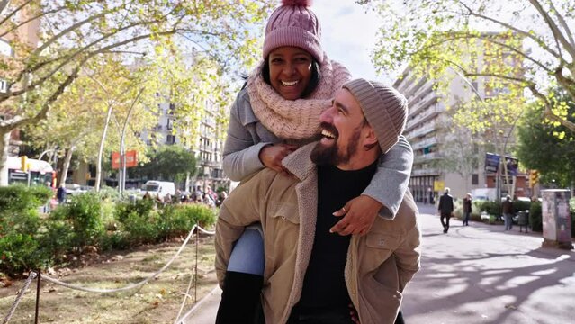 Happy young multiethnic couple in love doing piggyback outdoors in the city, smiling looking at camera.