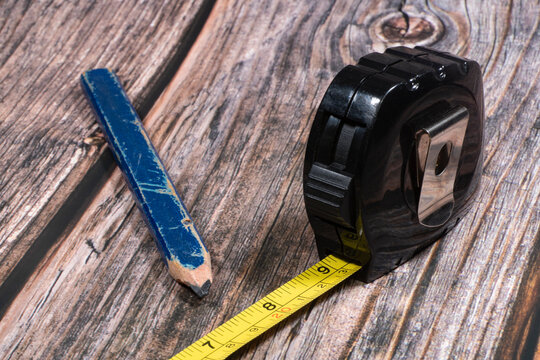 A close up image of a yellow carpenters tape measure and wooden pencil.