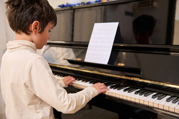 Rear view of a teenage boy pianist musician practicing on chord instrument, pianist playing piano indoors.