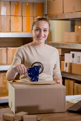 Smiling female entrepreneur packing parcel using tape dispenser. Woman preparing the product box for delivery to customer. Online business, ecommerce and delivery concept