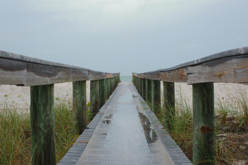 Mid level view out leading lines of Treasure Island Florida beach access bridge  with reflections of water . Green grass  beach and sand out the sides with water in distance. 