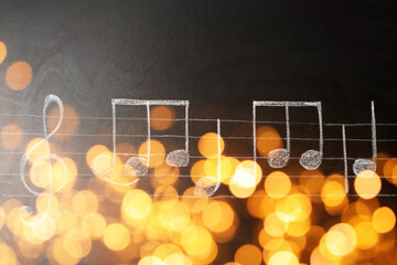 Christmas and New Year music. Chalked music notes on blackboard, bokeh effect