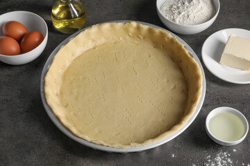 Quiche pan with fresh dough and ingredients on dark grey table, closeup