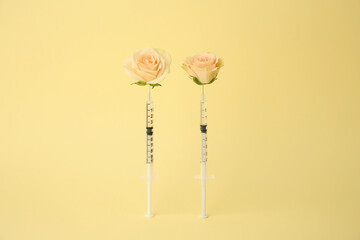 Medical syringes and rose flowers on pale yellow background