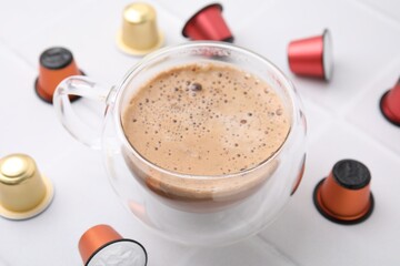 Cup of coffee and capsules on white tiled table, closeup