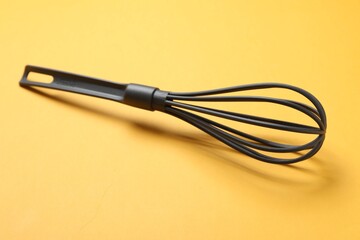 Plastic whisk on yellow background. Kitchen tool