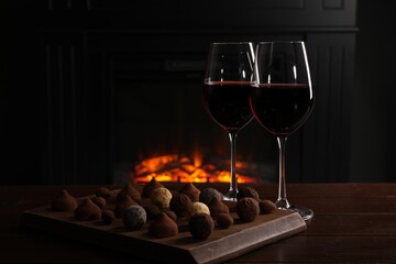 Red wine and chocolate truffles on wooden table against fireplace
