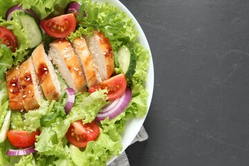 Delicious salad with chicken and vegetables on black table, top view. Space for text