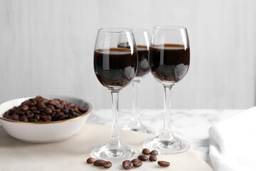 Glasses of coffee liqueur and beans on white table