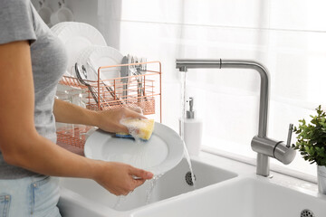 Woman washing plate at sink in kitchen, closeup