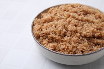 Tasty wheat porridge in bowl on white tiled table, closeup. Space for text