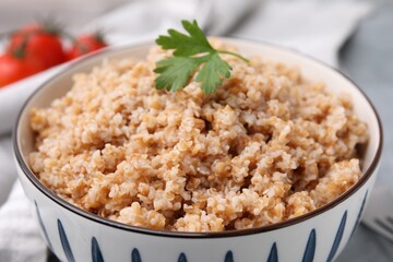 Tasty wheat porridge with parsley in bowl on table, closeup