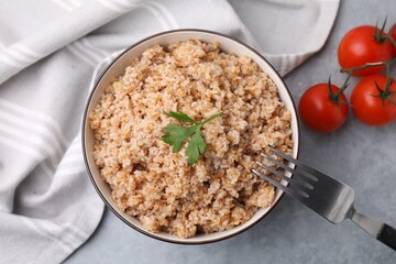 Tasty wheat porridge with parsley and tomatoes in bowl on grey table, flat lay