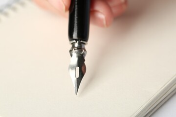 Woman with fountain pen above light paper, closeup