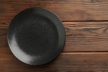 Beautiful black ceramic plate on wooden table, top view. Space for text