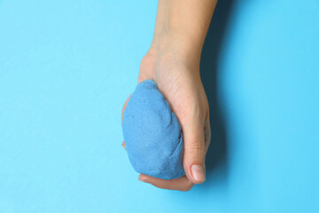 Woman playing with kinetic sand on light blue background, top view