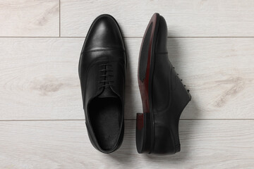 Pair of black leather men shoes on light wooden floor, top view