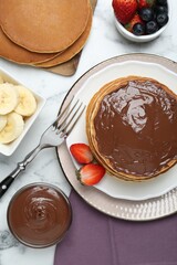 Tasty pancakes with chocolate paste, berries and fork on white marble table, flat lay