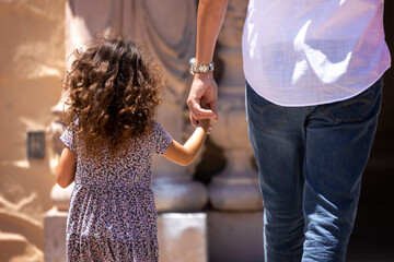 Child holding parents hand while walking outside.