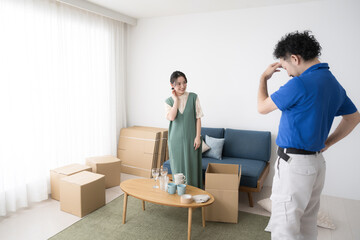 Wide-angle photo of a young woman who has not finished packing on moving day and a male contractor worker who is in trouble.