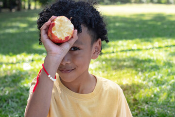African boy shows off an apple that has bite marks or nicks from his bite, at the park on a bright summer day, looking at camera