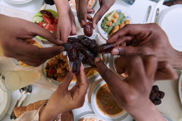 In a poignant close-up, the diverse hands of a Muslim family delicately grasp fresh dates, symbolizing the breaking of the fast during the holy month of Ramadan, capturing a moment of cultural unity